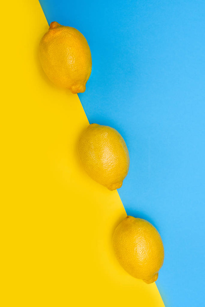 Kolme keltaista sitruunaa peräkkäin kelta-sinisellä pohjalla. Näkymä ylhäältä
. - Valokuva, kuva