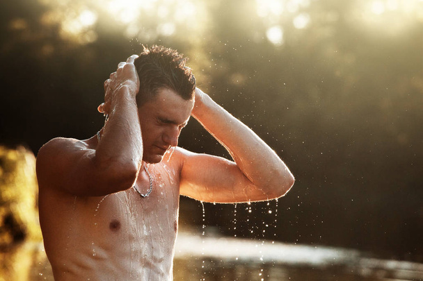 młody człowiek jest stały w rzece i mycia twarzy przed zachód słońca. Człowiek z gołymi tułowia stojąc w wodzie. - Zdjęcie, obraz