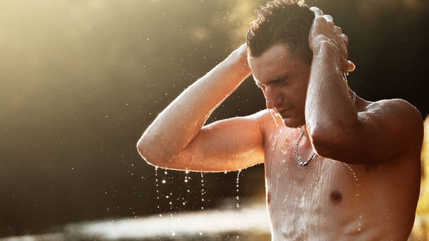 若い男は川に立って、夕日に対する彼の顔を洗います。水に立っている裸の胴体を持つ男. - 写真・画像