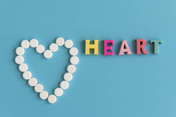 Heart concept on a blue background. Heart of white pills on a blue background. Heart inscription. - Фото, изображение