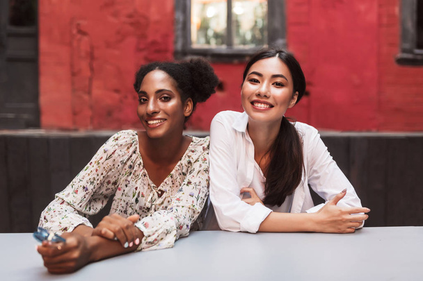 Dvě krásné usměvavé dívky šťastně při pohledu neveřejně trávit čas společně útulném dvoře kavárny - Fotografie, Obrázek