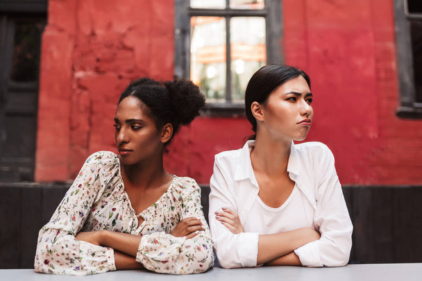 Dos mujeres jóvenes ofendidas por ech otros tristemente mirando a un lado pasar tiempo juntos en el patio de la cafetería
 - Foto, Imagen