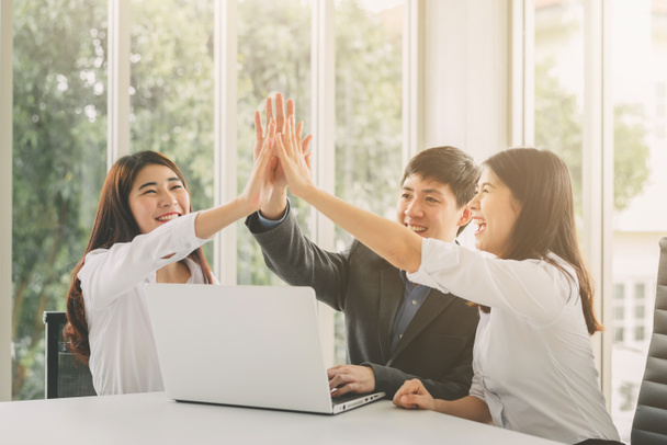 Gropu of young Asian business people giving high five to celebrate success on working project in meeting room - Photo, Image