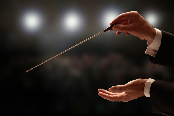 Dirigent dirigiert ein Orchester mit Publikum im Hintergrund - Foto, Bild