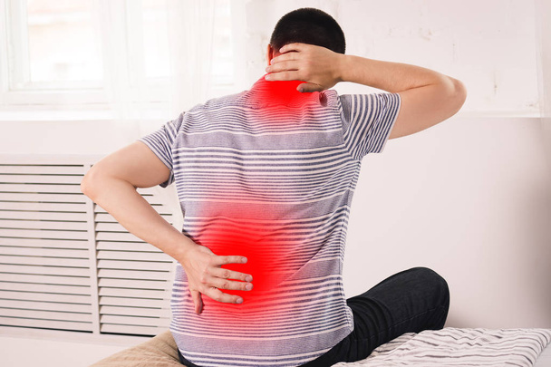 Neck pain, man suffering from backache at home, painful area highlighted in red - Photo, Image