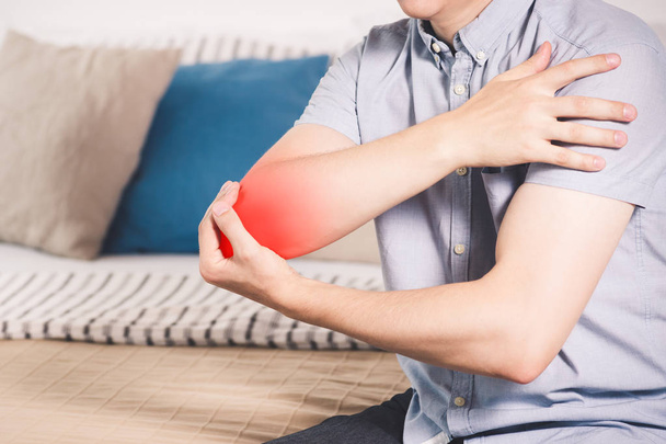 Man suffering from pain in elbow at home, joint inflammation, painful area highlighted in red - 写真・画像