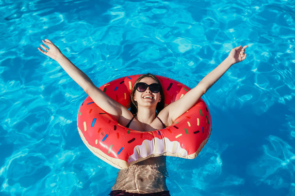 Beautiful young woman with pink donut circle have rest  in blue swimming pool - Fotografie, Obrázek