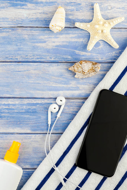 kreatives flaches Lagekonzept für Sommerreisen. Draufsicht auf Strandtuch Smartphone Muscheln Seesterne auf pastellblauen Holzplanken Hintergrund mit Kopie Raum Attrappe Vorlage für Text - Foto, Bild