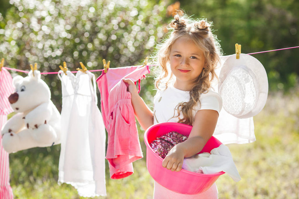 Cute little girl hanging out laundry outdoors - Zdjęcie, obraz