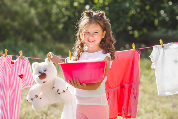 Linda niña colgando de la ropa al aire libre
 - Foto, imagen