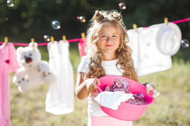 Söpö pieni tyttö ripustaa pyykkiä ulkona
 - Valokuva, kuva