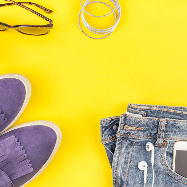 Flat lay of suede shoes, blue jeans, grey hat, cactus and smartphone headphones on bold yellow paper background with copy space. Overhead view of woman casual outfit. Square hipster look top view - Photo, Image