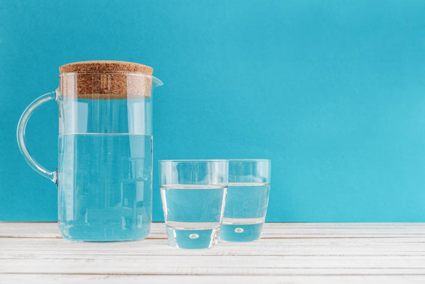 Jug and two glass with clear  water on blue background - Foto, Imagen