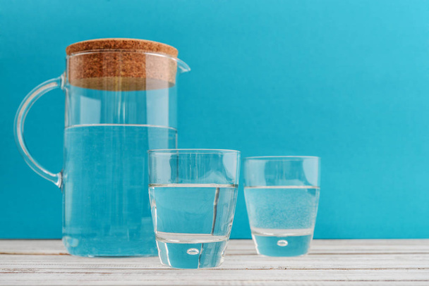 Jug and two glass with clear water on blue background - Фото, зображення