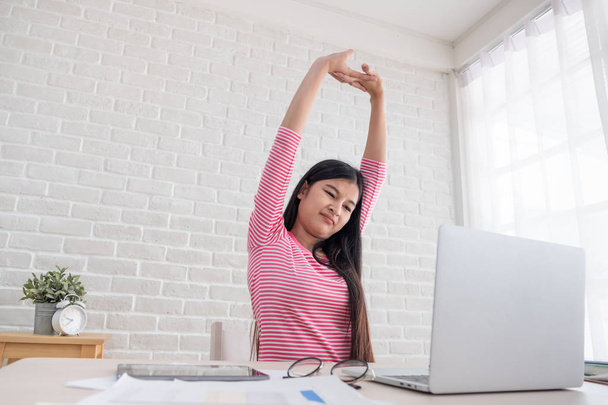 Asian woman stretching arm up when working on laptop at white brick wall in home.Work at home concept.relax after hard work - Foto, Imagen