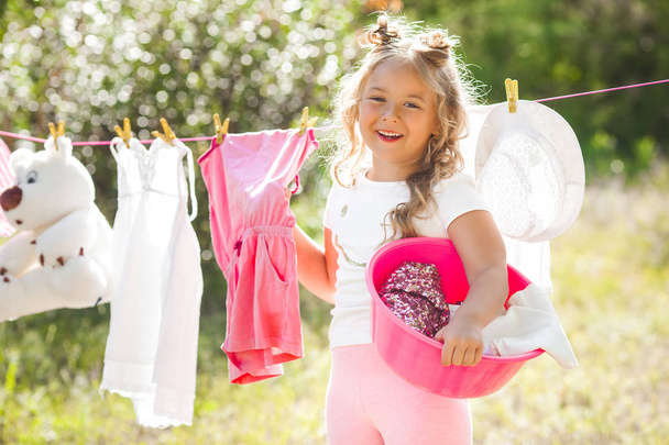 Linda niña colgando de la ropa al aire libre
 - Foto, imagen