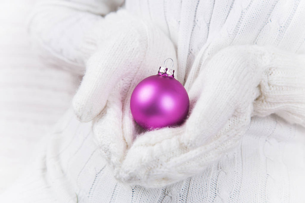 Manos en manoplas de punto blanco sosteniendo brillante bola de Navidad carmesí. Banner de Año Nuevo
. - Foto, imagen