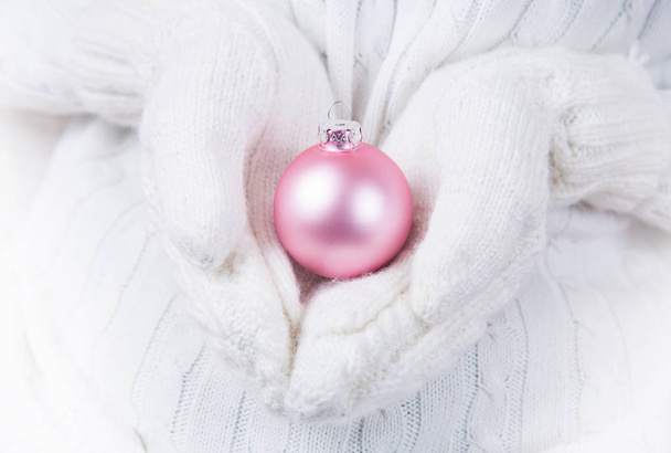 光るピンク クリスマス ボールを保持している白のニットのミトンで手。新年バナー. - 写真・画像