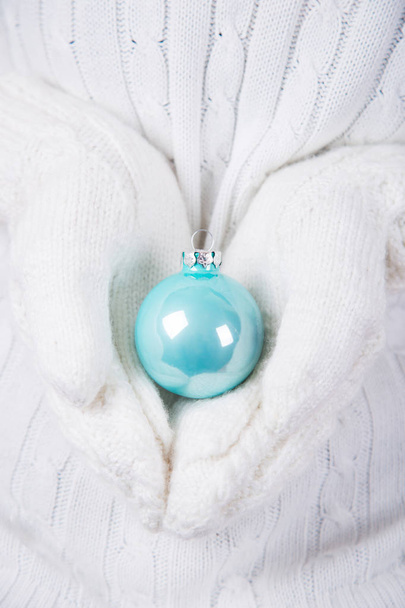 Manos en manoplas de punto blanco sosteniendo brillante bola de Navidad azul. Banner de Año Nuevo
. - Foto, imagen
