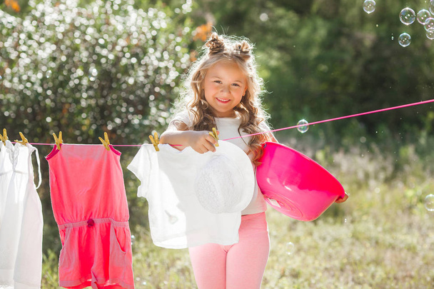 Cute little girl hanging out laundry outdoors - Photo, Image