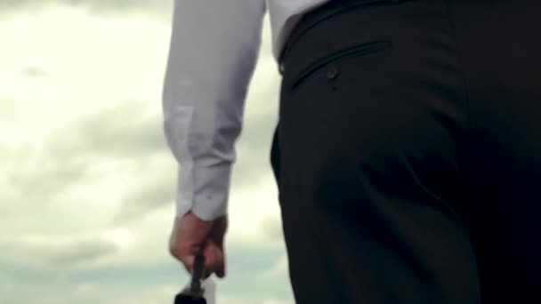 Businessman is walking along field with briefcase in his hand against background of dark clouds - Footage, Video