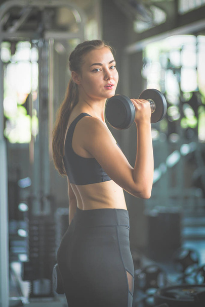 Fit beautiful young woman caucasian posing at the camera in sportswear. Young woman holding dumbbell during an exercise class in a gym. Healthy sports lifestyle, Fitness concept. - Fotó, kép