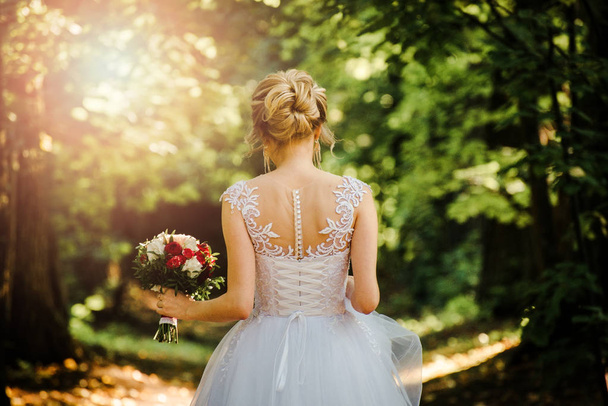 back of the bride against the background of foliage and sunlight with shallow depth of field - Фото, изображение