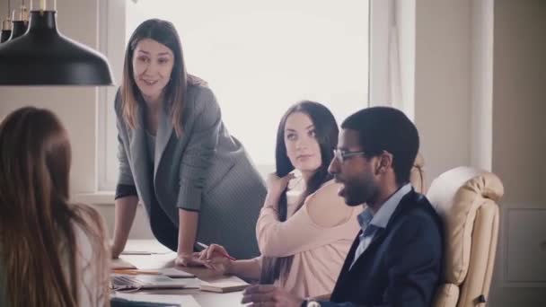 Successful attractive businesswoman encourages multiethnic team. Young female boss leading office meeting by the table. - Materiał filmowy, wideo
