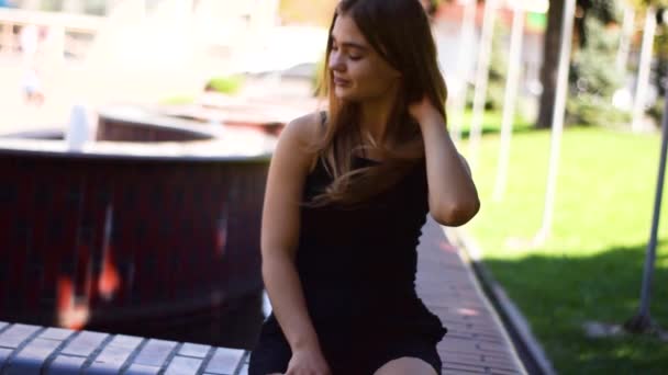 Young blond woman sitting on a bench and smiling - Felvétel, videó