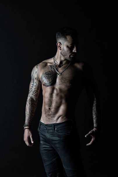 Fashion model with tattoo in jeans. Tattooed man show sexy muscular torso. Sportsman with six pack and ab. Bodybuilder with biceps and triceps. Bodycare with fitness and sport in vintage filter - Foto, afbeelding