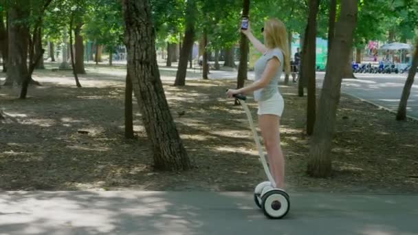 Girl in white shorts, riding a Segway on a clear sunny day. summer park and sun glare. 4k, slow-motion shooting, stadikam shot - Filmati, video
