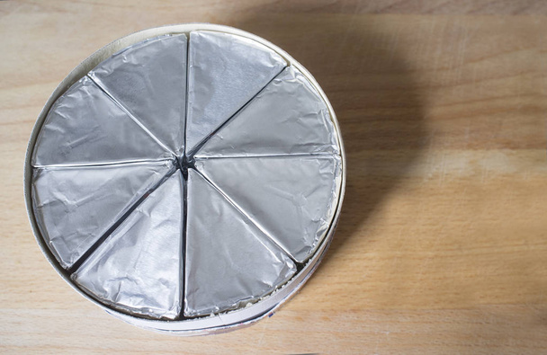 Caixa de papelão redonda com queijo derretido em folha de alumínio sobre mesa de madeira. Vista superior
 - Foto, Imagem