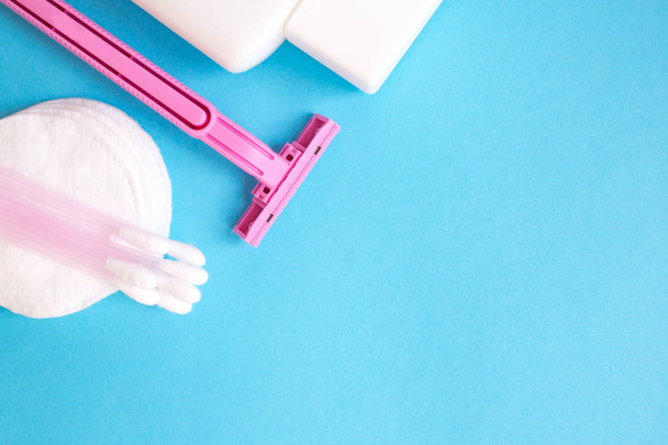 top view personal care products. white bottle, pink razor, ear sticks, cotton pads, toothbrush on blue background. copy space - Foto, afbeelding