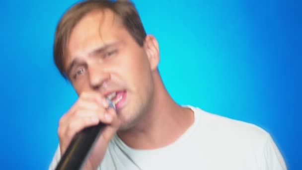 ένας τρελός αστεία νεαρός άνδρας τραγουδά τραγούδια σε ένα μικρόφωνο. χρώμα φόντου, γκρο πλαν. 4k, αργή κίνηση - Πλάνα, βίντεο