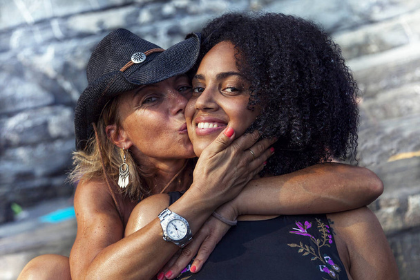 couple of beautiful women of different ethnicity while hugging on beach vacation - Photo, Image