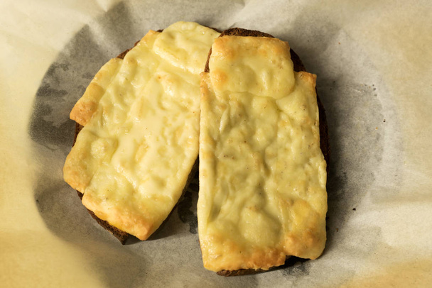Два ломтика жареного сыра на поджаренном ржаном хлебе на хлебобулочной бумаге - закуски, плавленный сыр
 - Фото, изображение