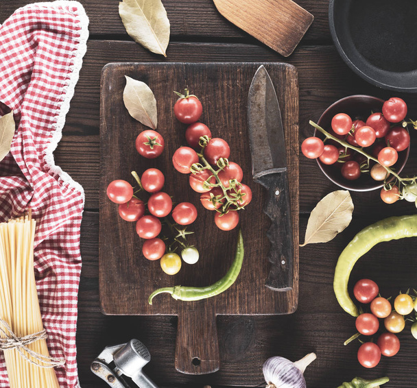tábua de corte de madeira com uma faca e tomates cereja vermelho fresco, ao lado de um pacote amarrado de espaguete cru longo
 - Foto, Imagem