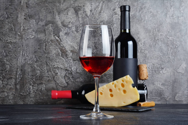Red wine bottles with glass and cheese for tasting in cellar on gray concrete background - Foto, afbeelding