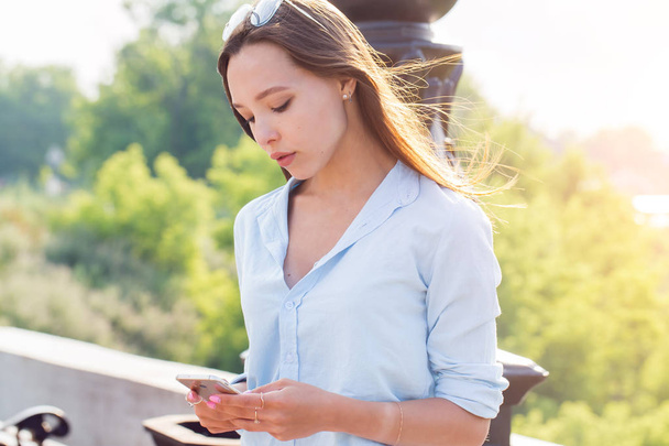 Beautiful young brunette woman with smartphone on hand in the Park, outdoors, closeup portrait - 写真・画像