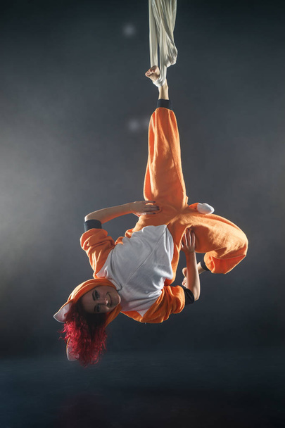 red-haired circus girl making fanny trick on air silk in orange fox pajamas - Zdjęcie, obraz