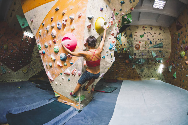 The climber trains on the climbing wall. A woman trains to climb on an artificial relief. A slender girl goes in for sports. - Photo, Image