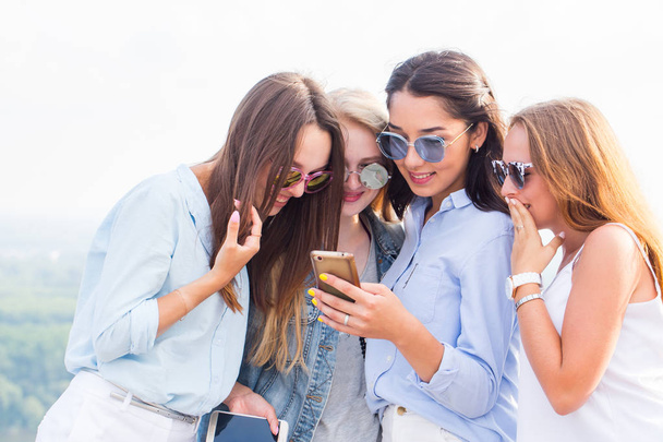 Use of smartphones, the Internet, applications and messages. A group of beautiful girls look at the phone girlfriend and laugh, surprised - Foto, imagen