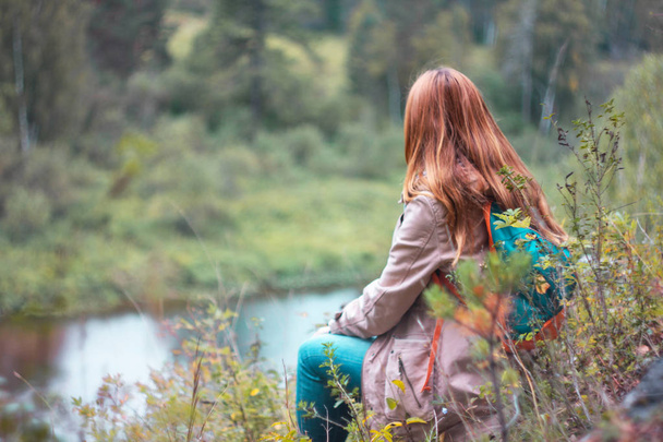 Tyttö matkustava punainen pitkät hiukset istuu ja katselee villi luonto
 - Valokuva, kuva