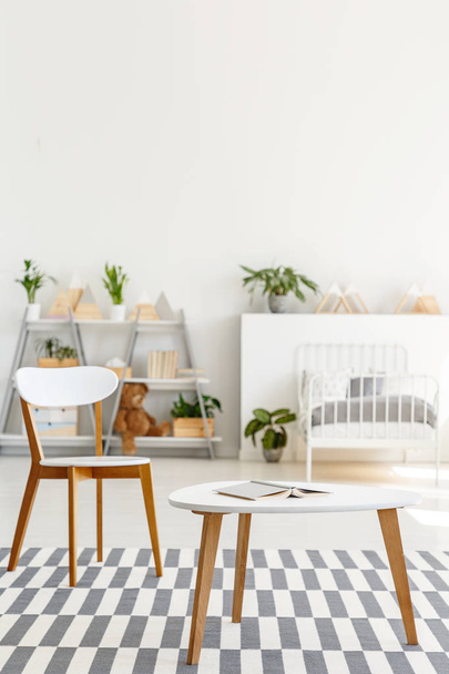 Tisch und Stuhl auf gemustertem Teppich im Innenraum eines weißen Kinderzimmers mit Pflanzen. echtes Foto mit unscharfem Hintergrund - Foto, Bild