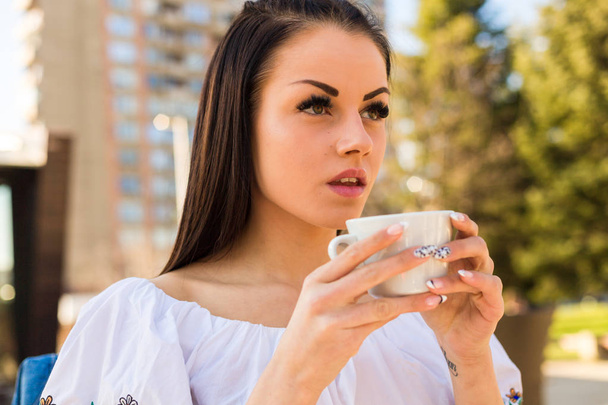 Kaunis nuori nainen juo kahvia ulkona - Valokuva, kuva