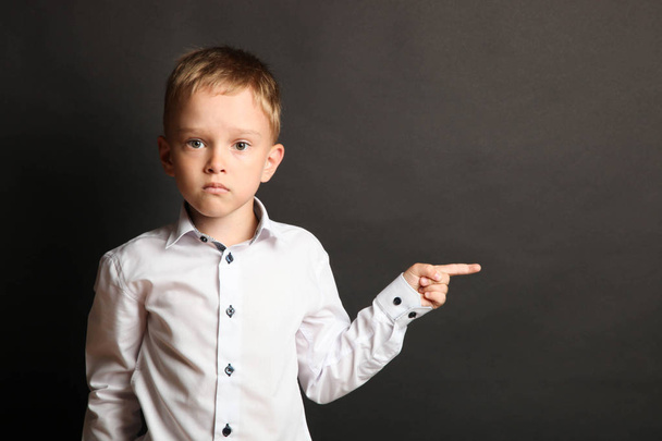 Schoolboy in white shirt shows finger on black background. Concept school. - Фото, изображение