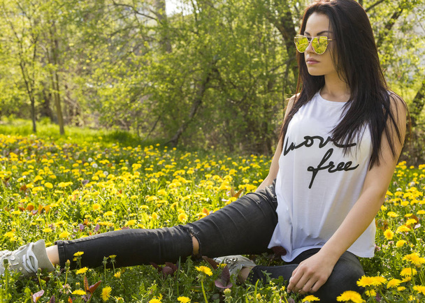 stylish young woman sitting on green meadow with blooming dandelions - Foto, Imagem