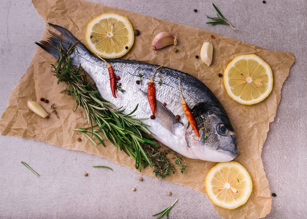 Fresh dorado fish. Dorado and cooking ingredients - rosemary, spices, lemon, garlic, thyme, herbs. Cooking concept. On light stone background. Top view, view from above. - Photo, image