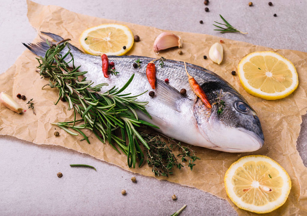 Fresh dorado fish. Dorado and cooking ingredients - rosemary, spices, lemon, garlic, thyme, herbs. Cooking concept. On light stone background. - Foto, imagen