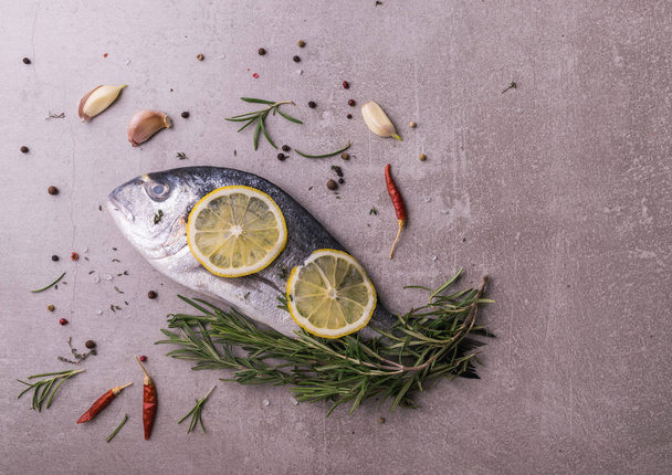 Fresh dorado fish. Dorado and cooking ingredients - rosemary, spices, lemon, garlic, thyme, herbs. Cooking concept. On light stone background. top view, view from above. - Foto, immagini
